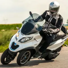 Kierowca w kasku na białym Piaggio MP3 500, pokonujący zakręt na drodze. Czy wady tego modelu są widoczne?