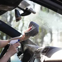 Kobieta czyści zaparowane szyby w samochodzie. Czy to przez ciepły czy zimny nawiew?