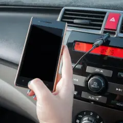 Dłoń trzyma smartfon podłączony kablem do radia samochodowego. Wybrano wejście aux.