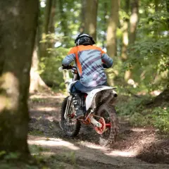 Motocyklista w kasku i kolorowej bluzie pędzi po leśnym torze. Zastanawiasz się, prawo jazdy na crossa od ilu lat jest potrzebne, by poczuć taką wolność?