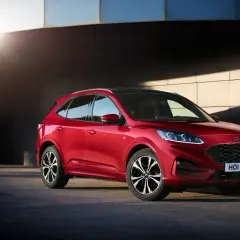 Czerwony Ford Kuga prezentuje swoje dynamiczne linie i imponujące ford kuga wymiary. Stylowy SUV na tle nowoczesnej architektury.