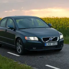 Ciemnozielone Volvo S40 jedzie drogą przez pole rzepaku. Poznaj jego wymiary i możliwości.