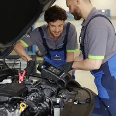 Mechanicy diagnozują przyczynę delikatnego szarpania podczas jazdy ze stałą prędkością, sprawdzając akumulator za pomocą testera.