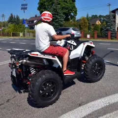 Mężczyzna na quadzie bez kasku, naraża się na mandat. Słońce świeci, droga pusta, ale przepisy są jasne.