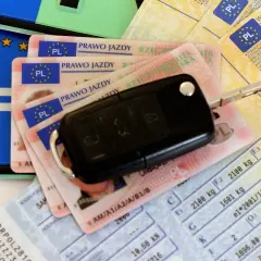Kluczyki do auta i dokumenty, w tym prawo jazdy. Czy prawo jazdy jest bezterminowe? Na zdjęciu widać też dowód rejestracyjny i tablicę.