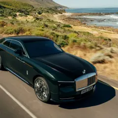 Elegancki, zielony Rolls Royce elektryczny sunie po malowniczej drodze nad oceanem.