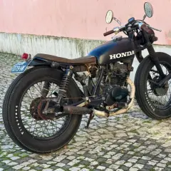 Czarny customowy motor 125 bez prawa jazdy, z brązowym siedzeniem i wydechem owiniętym taśmą, stoi na bruku.