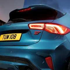 Tylna część sportowego Forda Focus ST 2025 w kolorze niebieskim, z podświetlonymi światłami i czerwonym emblematem ST.