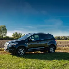 Czarny Ford Kuga na tle pola i drzew. Zastanawiasz się nad jego **ford kuga spalanie**?