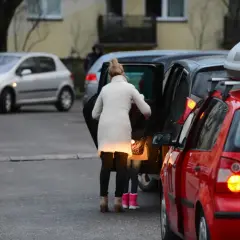 Kobieta z dzieckiem wsiada do samochodu, tworząc zator. Miejsce, gdzie nie można parkować, bo blokuje ruch.