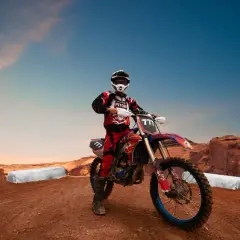Motocyklista w stroju crossowym na tle pustynnych skał. Idealne miejsce, gdzie można jeździć crossem i poczuć wolność.
