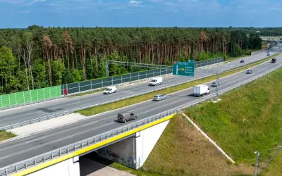 Droga ekspresowa S17 z zielonymi ekranami akustycznymi i lasem w tle. Ruch samochodowy na wielopasmowej trasie.