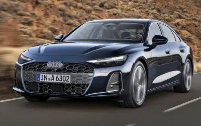 Ciemnoniebieskie Audi A6 C9 z nowoczesnym grillem i światłami LED jedzie po pustynnej drodze.