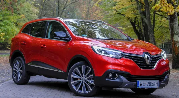 Czerwony Renault Kadjar na tle jesiennego lasu. Wady tego modelu to m.in. przeciętne wyciszenie i twarde zawieszenie.
