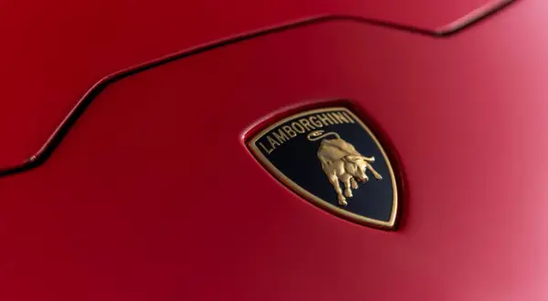 Złote logo Lamborghini z bykiem na czerwonym tle, symbol luksusowych marek samochodów.