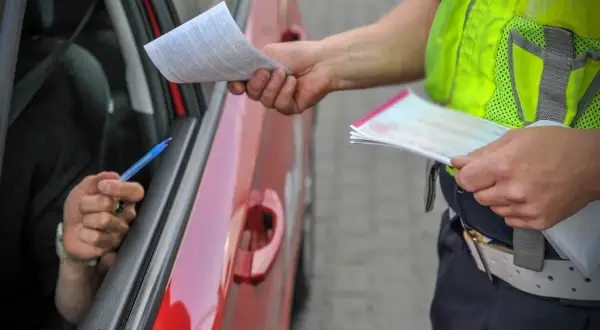 Policjant w kamizelce odblaskowej wręcza kierowcy dokumenty. Kierowca trzyma długopis, gotowy do podpisania. Ważne jest, ile czasu na zapłacenie mandatu.
