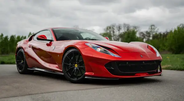 Czerwony, luksusowy samochód sportowy Ferrari 812 Superfast na tle pochmurnego nieba i zieleni.