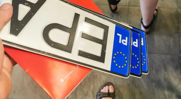 Kilka nowych tablic rejestracyjnych PL leży na czerwonym podkładzie.
