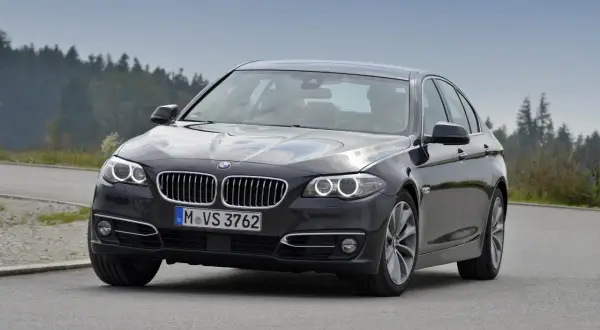 Ciemnoszary sedan BMW F10 na drodze, z widokiem na las. Idealne wymiary dla komfortowej podróży.