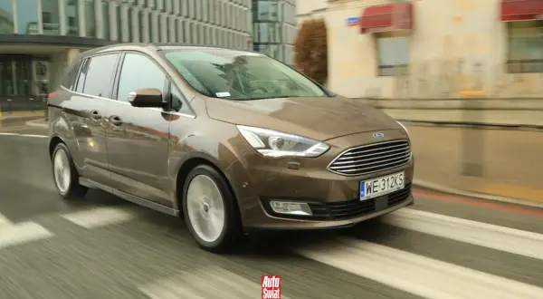 Brązowy Ford Grand C-Max w ruchu miejskim, z widocznymi kroplami deszczu na karoserii i rozmazanym tłem.