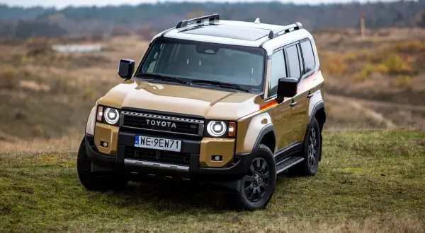 Złoty Toyota Land Cruiser z czarnymi dodatkami i relingami dachowymi stoi na trawiastym wzgórzu.