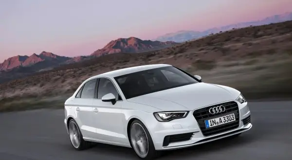 Białe Audi A3 jedzie po drodze w górach. Jego lekka konstrukcja i dynamiczny wygląd podkreślają jego sportowy charakter.