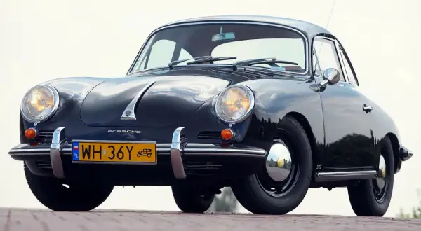 Czarne, zabytkowe auto Porsche z lat 50. XX wieku, z charakterystycznym przodem i żółtą tablicą rejestracyjną.