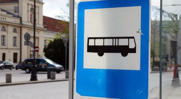 Znak przystanku autobusowego. Czy autobus ma pierwszeństwo? Na ulicy widać samochody i budynek.