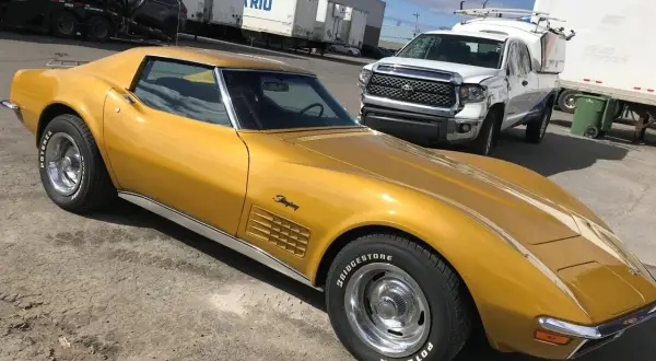 Złoty Chevrolet Corvette Stingray, jeden z klasycznych, sportowych aut, zaparkowany obok białej ciężarówki.