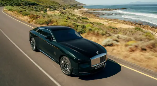Elegancki, zielony Rolls Royce elektryczny sunie po malowniczej drodze nad oceanem.