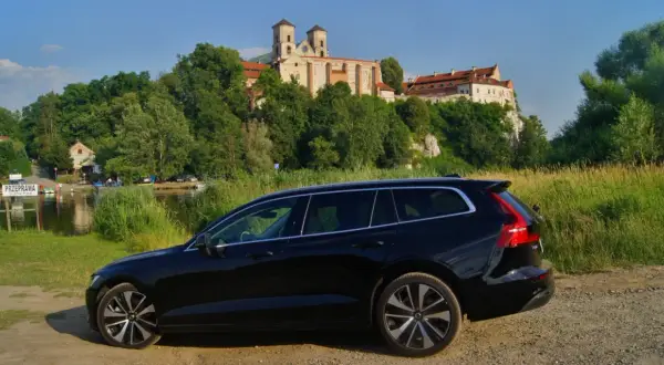 Czarne Volvo V60 na tle malowniczego klasztoru i rzeki. Idealne na wakacyjne podróże, gdzie niskie volvo v60 spalanie pozwoli cieszyć się widokami.