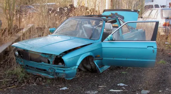 Turkusowy, zniszczony samochód na złomowisku. Drzwi i maska otwarte, jakby ktoś właśnie zaczął zastanawiać się, jak zezłomować auto.