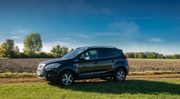 Czarny Ford Kuga na tle pola i drzew. Zastanawiasz się nad jego **ford kuga spalanie**?