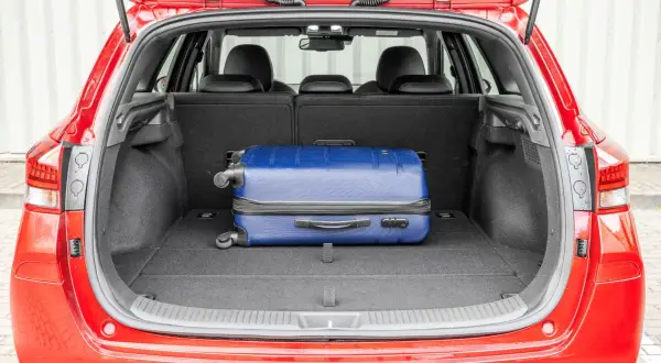 Otwarty bagażnik czerwonego Hyundai i30 kombi z niebieską walizką. Sprawdź pojemność bagażnika na podróż!