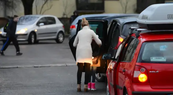 Kobieta z dzieckiem wsiada do samochodu, tworząc zator. Miejsce, gdzie nie można parkować, bo blokuje ruch.