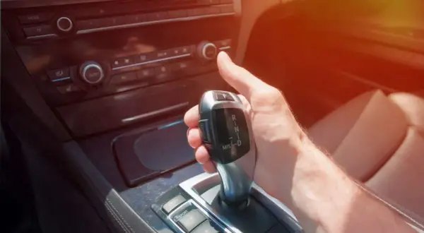 Dłoń kierowcy chwyta lewarek zmiany biegów, gotowa do wrzucenia wstecznego w automacie.