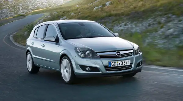 Srebrny Opel Astra GTC z kierowcą za kierownicą pokonuje zakręt na górskiej drodze.