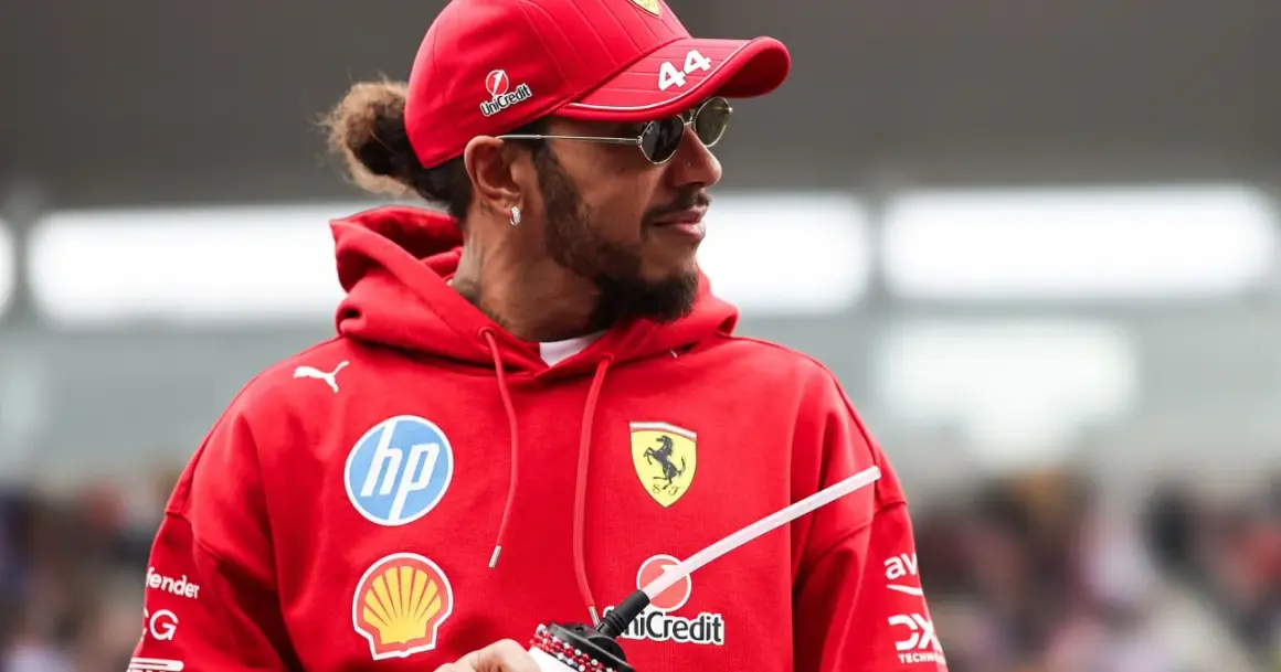 Hamilton, wielokrotny mistrz świata Formuły 1, w czerwonej bluzie z logo Ferrari i okularach przeciwsłonecznych.