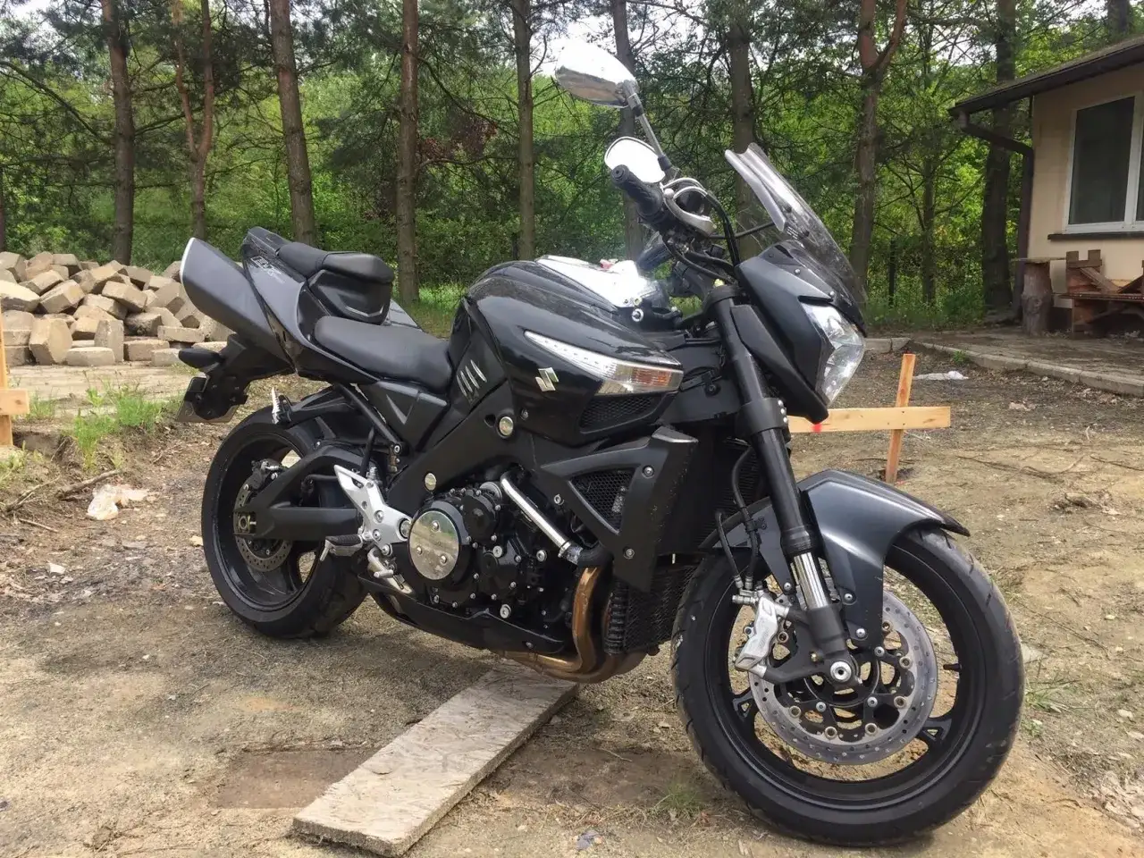 Czarny Suzuki B-King, potężny naked bike, gotowy na przygodę wśród drzew.