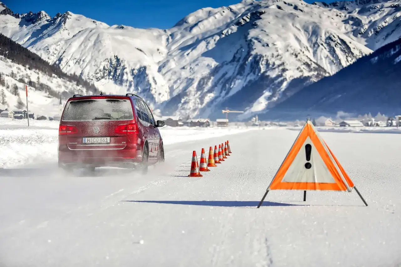 Czerwony Volkswagen Touran na śniegu, test opon zimowych. W tle ośnieżone góry i miasteczko.