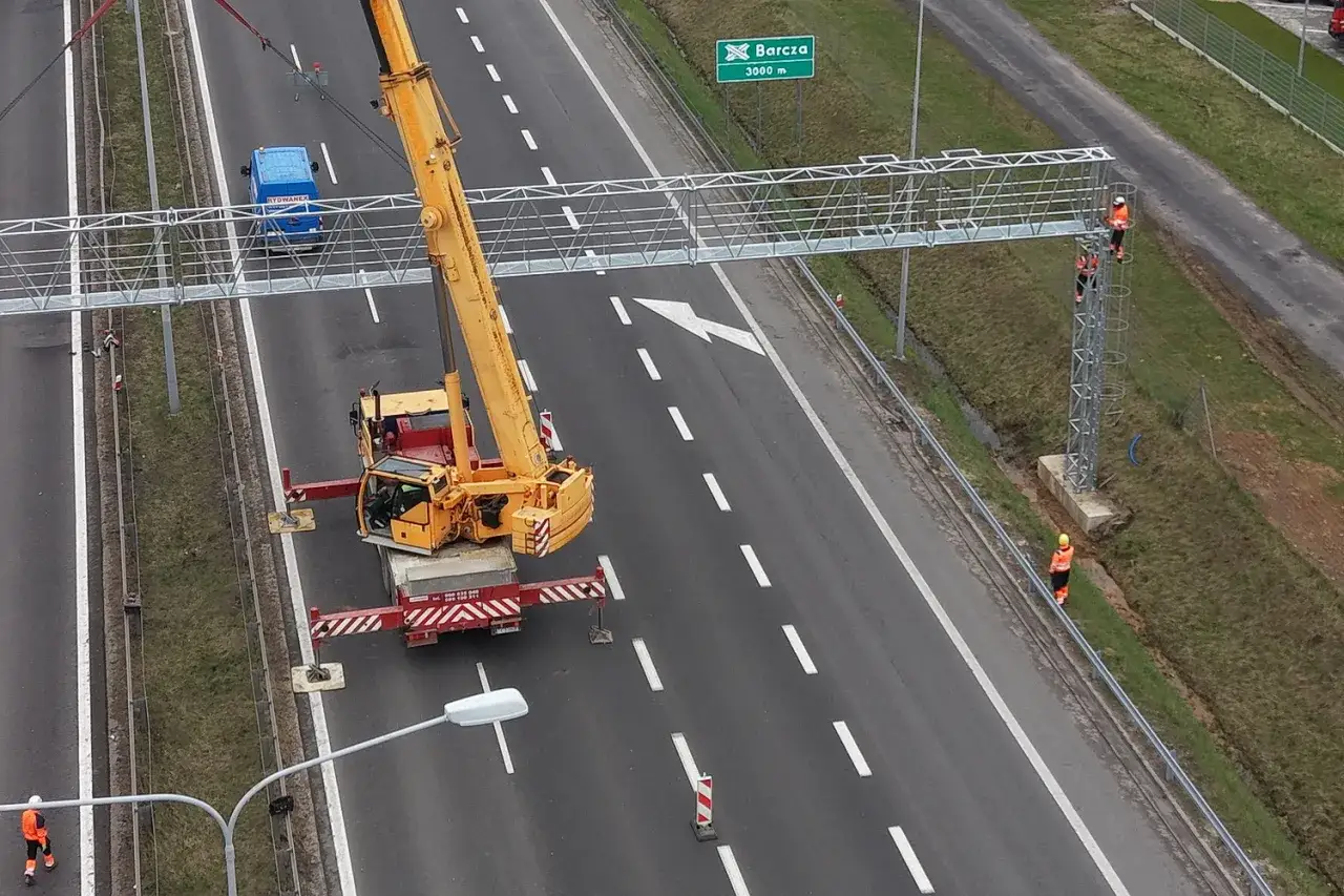 Montaż konstrukcji do odcinkowego pomiaru prędkości S7. Dźwig pomaga pracownikom w instalacji.