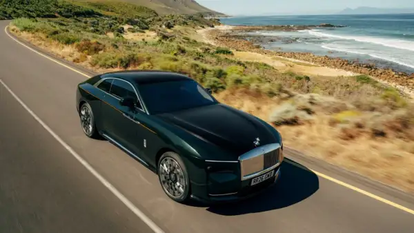 Elegancki, zielony Rolls Royce elektryczny sunie po malowniczej drodze nad oceanem.