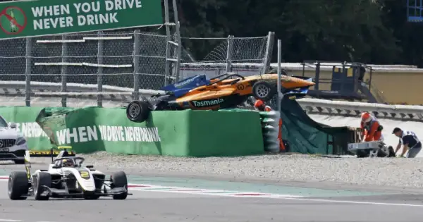 Wypadek bolidu F1 na torze Monza. Pomarańczowo-niebieski bolid leży na bandzie, ratownicy udzielają pomocy.